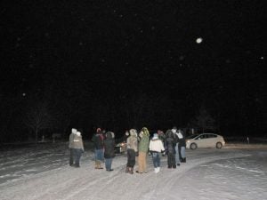 group of people standing in snow looking up at the moon